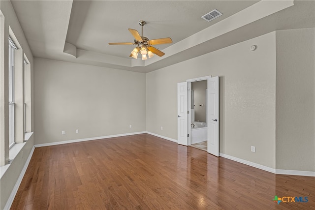 empty room featuring wood-type flooring, a raised ceiling, and ceiling fan