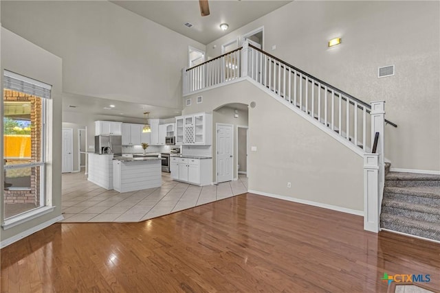 unfurnished living room featuring a towering ceiling, light hardwood / wood-style flooring, and ceiling fan