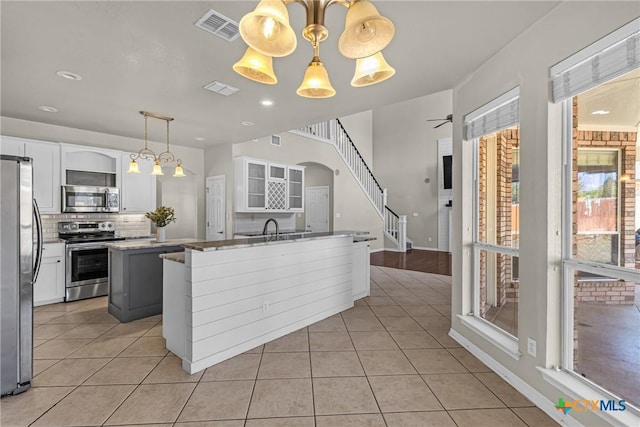 kitchen featuring ceiling fan with notable chandelier, stainless steel appliances, a kitchen island, white cabinetry, and hanging light fixtures