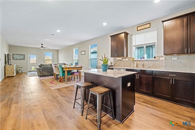 kitchen featuring dark brown cabinetry, tasteful backsplash, a kitchen island, light stone countertops, and light hardwood / wood-style floors