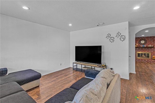 living room with a textured ceiling, hardwood / wood-style floors, and a brick fireplace