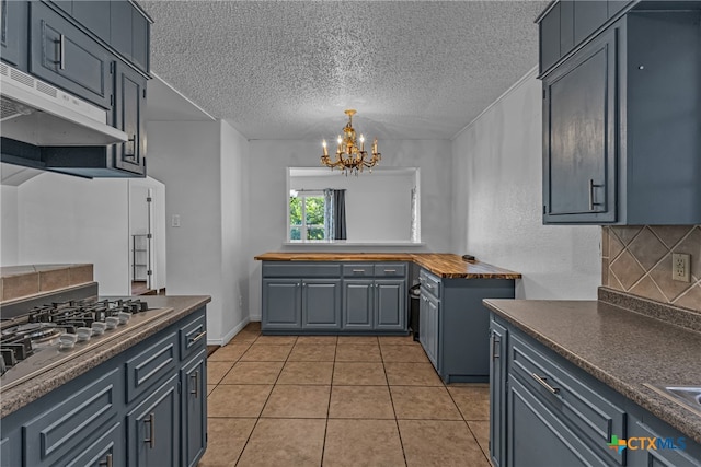 kitchen featuring stainless steel gas stovetop, decorative backsplash, a textured ceiling, a chandelier, and light tile patterned flooring