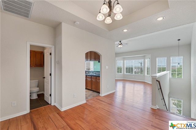 interior space with a tray ceiling, a textured ceiling, a notable chandelier, and light hardwood / wood-style floors