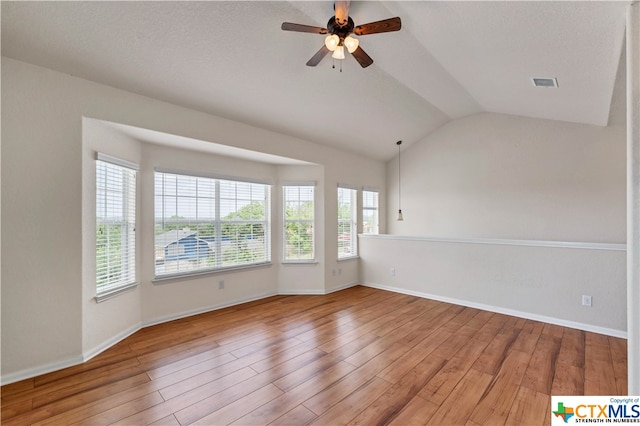 empty room with a textured ceiling, lofted ceiling, hardwood / wood-style flooring, and ceiling fan