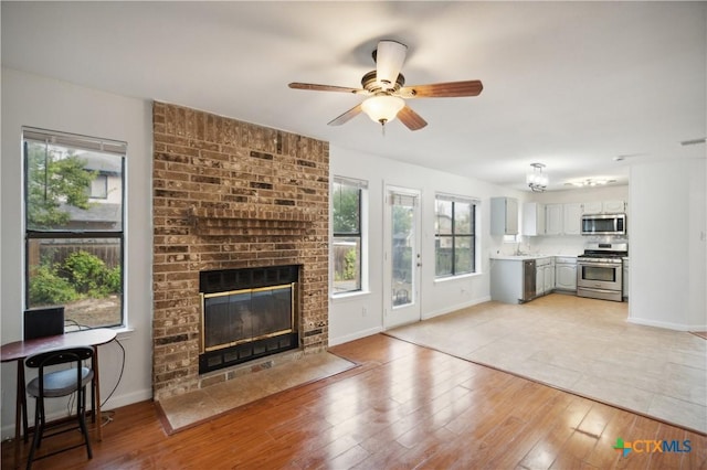 living room with light hardwood / wood-style floors, a brick fireplace, ceiling fan, and sink