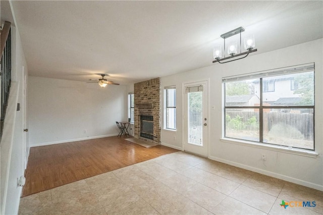 unfurnished living room featuring a fireplace, light tile patterned floors, and ceiling fan with notable chandelier