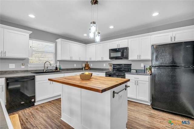 kitchen with wood finished floors, a sink, black appliances, butcher block countertops, and white cabinetry
