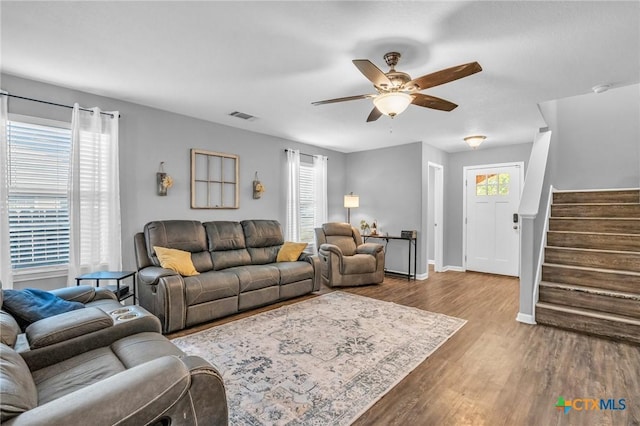 living area with stairway, wood finished floors, visible vents, baseboards, and ceiling fan