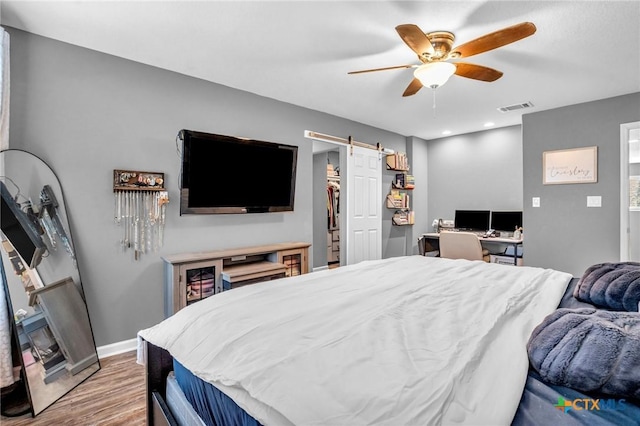 bedroom featuring a barn door, baseboards, visible vents, wood finished floors, and ceiling fan