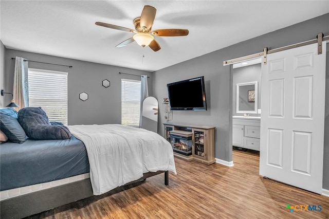 bedroom featuring a barn door, baseboards, wood finished floors, ceiling fan, and connected bathroom