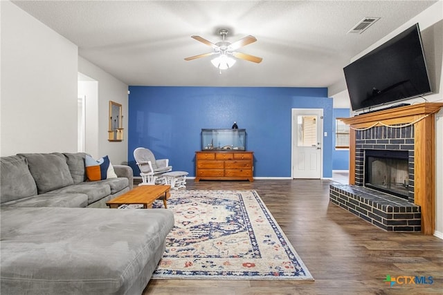 living room with a fireplace, ceiling fan, dark hardwood / wood-style flooring, and a textured ceiling