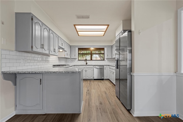 kitchen with stainless steel appliances, kitchen peninsula, gray cabinetry, light stone countertops, and light wood-type flooring