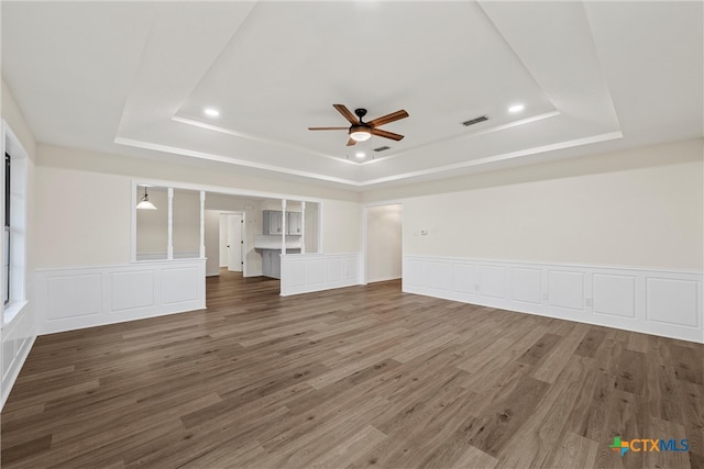 unfurnished living room with dark wood-type flooring, ceiling fan, and a raised ceiling