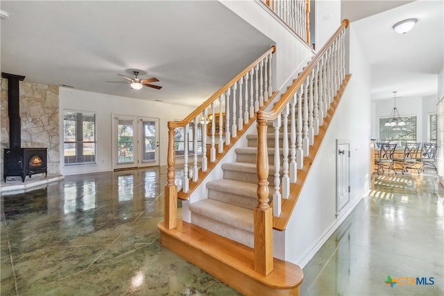 staircase with a wood stove, ceiling fan with notable chandelier, concrete flooring, and french doors