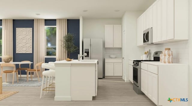 kitchen featuring light hardwood / wood-style flooring, a breakfast bar, white cabinetry, stainless steel appliances, and an island with sink