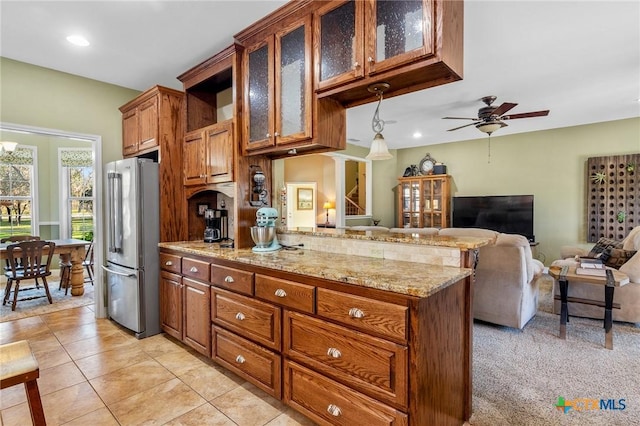 kitchen with hanging light fixtures, ceiling fan, stainless steel fridge, light stone countertops, and kitchen peninsula