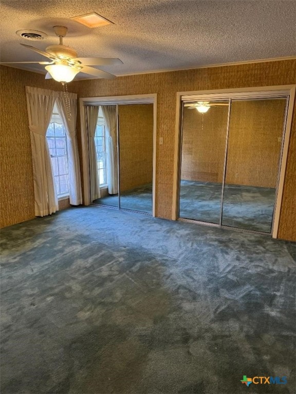 unfurnished bedroom featuring dark colored carpet, ornamental molding, two closets, and a textured ceiling