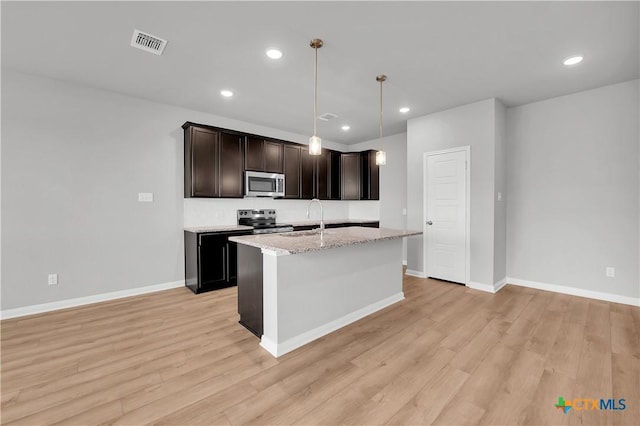 kitchen with sink, decorative light fixtures, appliances with stainless steel finishes, a kitchen island with sink, and light hardwood / wood-style floors