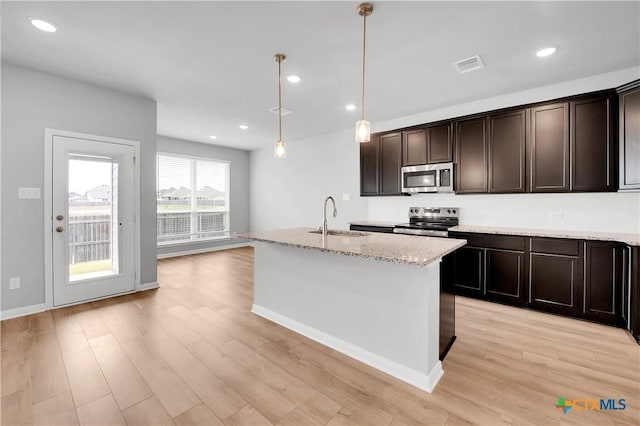 kitchen with appliances with stainless steel finishes, pendant lighting, sink, light stone counters, and a center island with sink