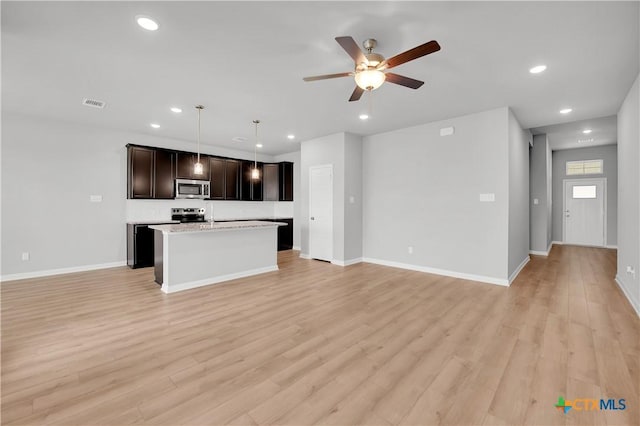 kitchen featuring stainless steel appliances, an island with sink, hanging light fixtures, and light wood-type flooring