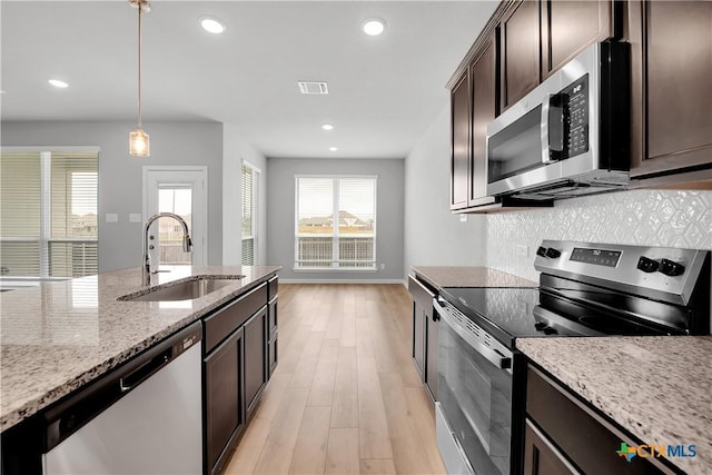 kitchen with decorative light fixtures, sink, stainless steel appliances, light stone countertops, and dark brown cabinets