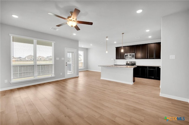 kitchen with stainless steel appliances, an island with sink, light hardwood / wood-style floors, and decorative light fixtures