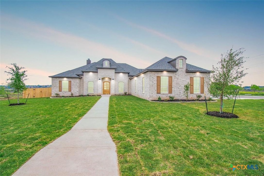 french country style house with brick siding, a chimney, fence, and a yard