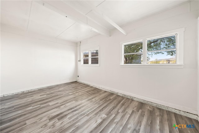 unfurnished room with beamed ceiling, a wealth of natural light, and hardwood / wood-style flooring