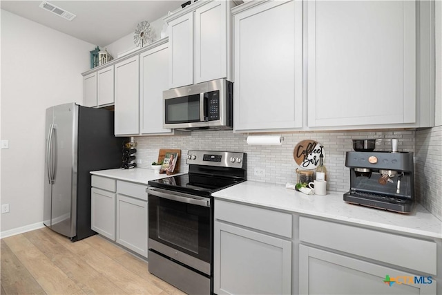 kitchen featuring appliances with stainless steel finishes, white cabinetry, backsplash, light stone counters, and light hardwood / wood-style floors