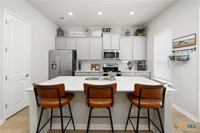 kitchen with sink, appliances with stainless steel finishes, a kitchen bar, and a kitchen island with sink