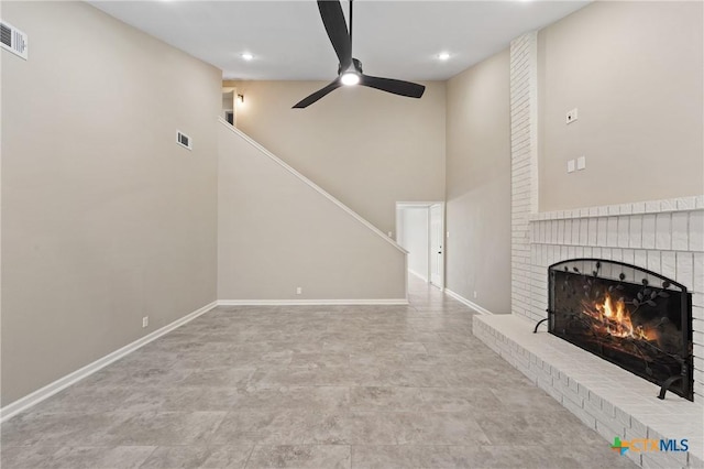 unfurnished living room featuring ceiling fan, a towering ceiling, and a fireplace