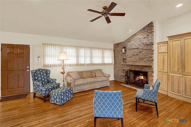 living room featuring vaulted ceiling, ceiling fan, a fireplace, and light hardwood / wood-style floors