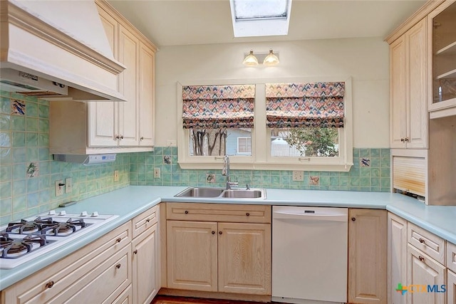 kitchen with sink, white appliances, premium range hood, backsplash, and a skylight