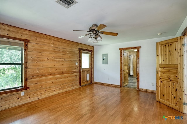 unfurnished room featuring ceiling fan, wood-type flooring, electric panel, and wood walls