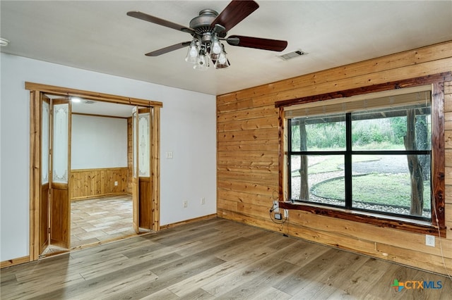 empty room featuring ceiling fan, light hardwood / wood-style flooring, and wood walls