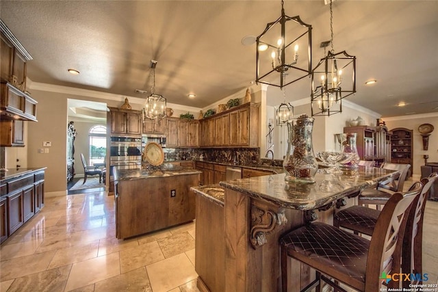 kitchen with a center island, backsplash, dark stone counters, a notable chandelier, and appliances with stainless steel finishes