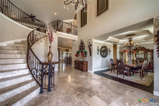 entryway with crown molding, baseboards, stairs, a tray ceiling, and an inviting chandelier