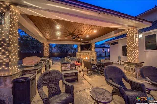 view of patio with exterior fireplace, fence, outdoor dining space, ceiling fan, and area for grilling