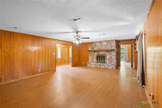 408 Royal Oak Dr, Victoria, TX 77905 - unfurnished living room with light wood-style flooring, wood walls, a ceiling fan, a textured ceiling, and a stone fireplace