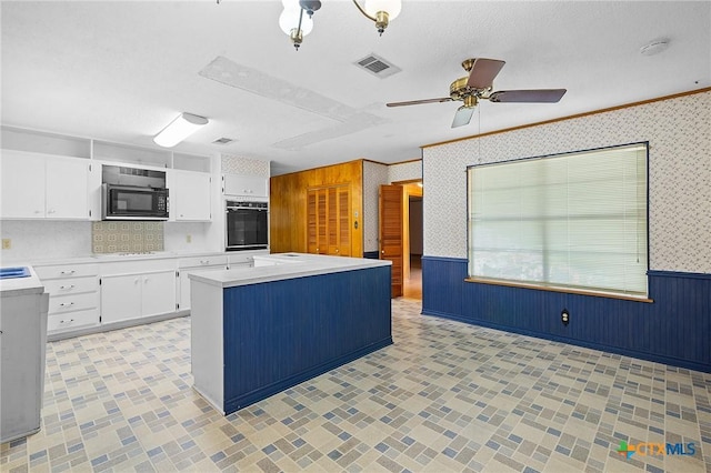 408 Royal Oak Dr, Victoria, TX 77905 - kitchen with black oven, light countertops, wainscoting, wallpapered walls, and white cabinetry