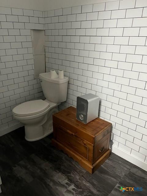 bathroom with toilet and tile walls