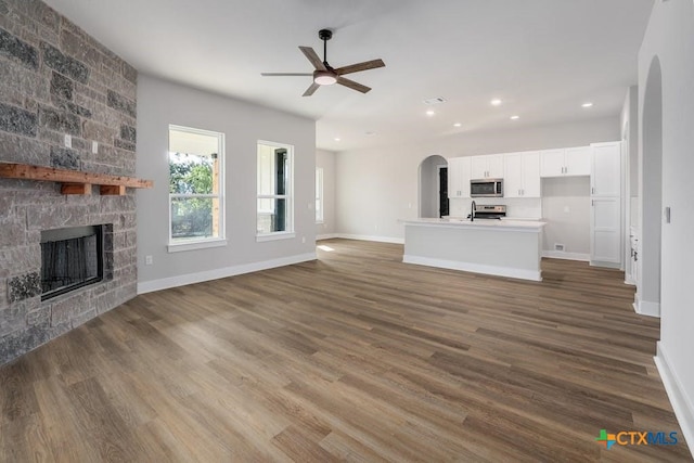 unfurnished living room with a stone fireplace, ceiling fan, and dark hardwood / wood-style floors