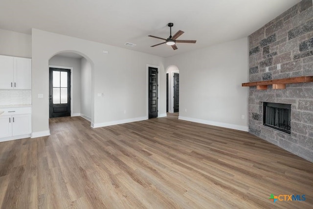 unfurnished living room with ceiling fan, a stone fireplace, and light wood-type flooring