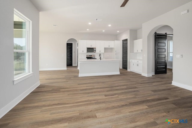 kitchen featuring white cabinetry, stainless steel appliances, a barn door, an island with sink, and wood-type flooring