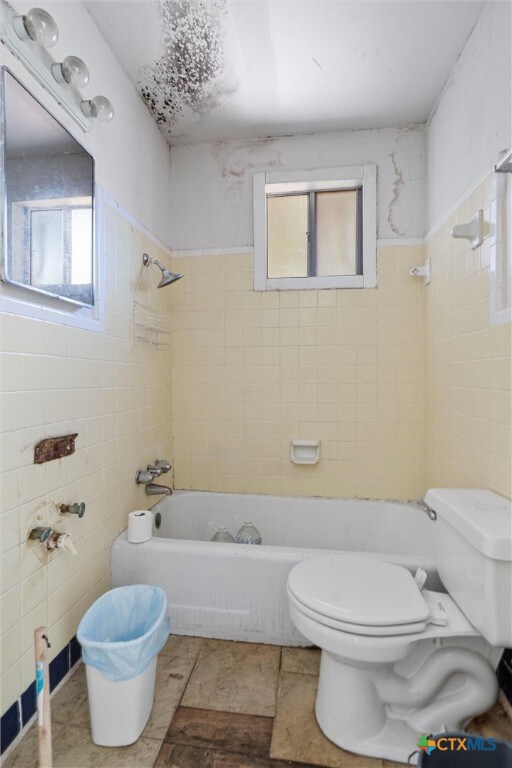 bathroom featuring a wealth of natural light, toilet, tile walls, and tiled shower / bath combo