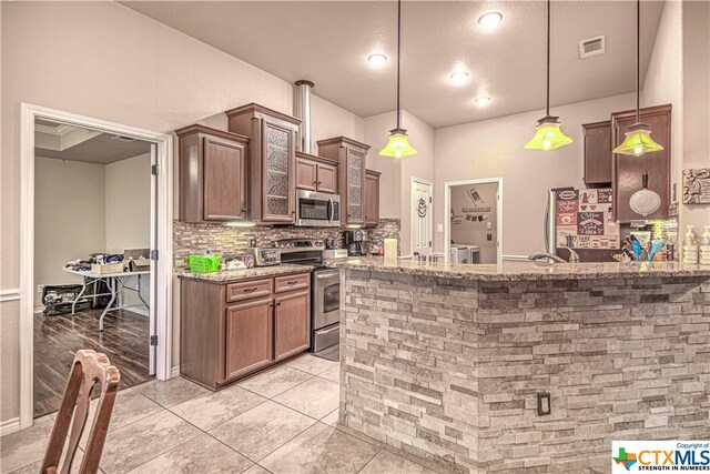 kitchen with light stone counters, hanging light fixtures, tasteful backsplash, light tile patterned flooring, and appliances with stainless steel finishes