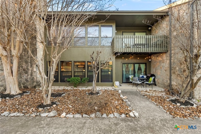 back of property with stone siding, a patio area, and a balcony