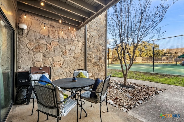 view of patio featuring a tennis court and fence