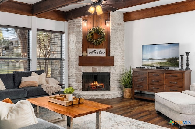 living area with dark wood-style floors, ceiling fan, beam ceiling, and a stone fireplace