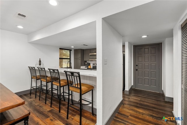 kitchen featuring stainless steel appliances, a peninsula, visible vents, a kitchen breakfast bar, and light countertops